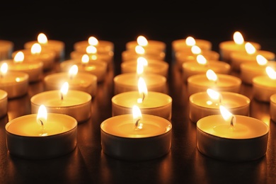 Photo of Wax candles burning on table in darkness, closeup