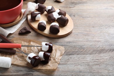 Delicious marshmallows covered with chocolate on wooden table, space for text