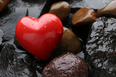 Red decorative heart on stones and water, closeup