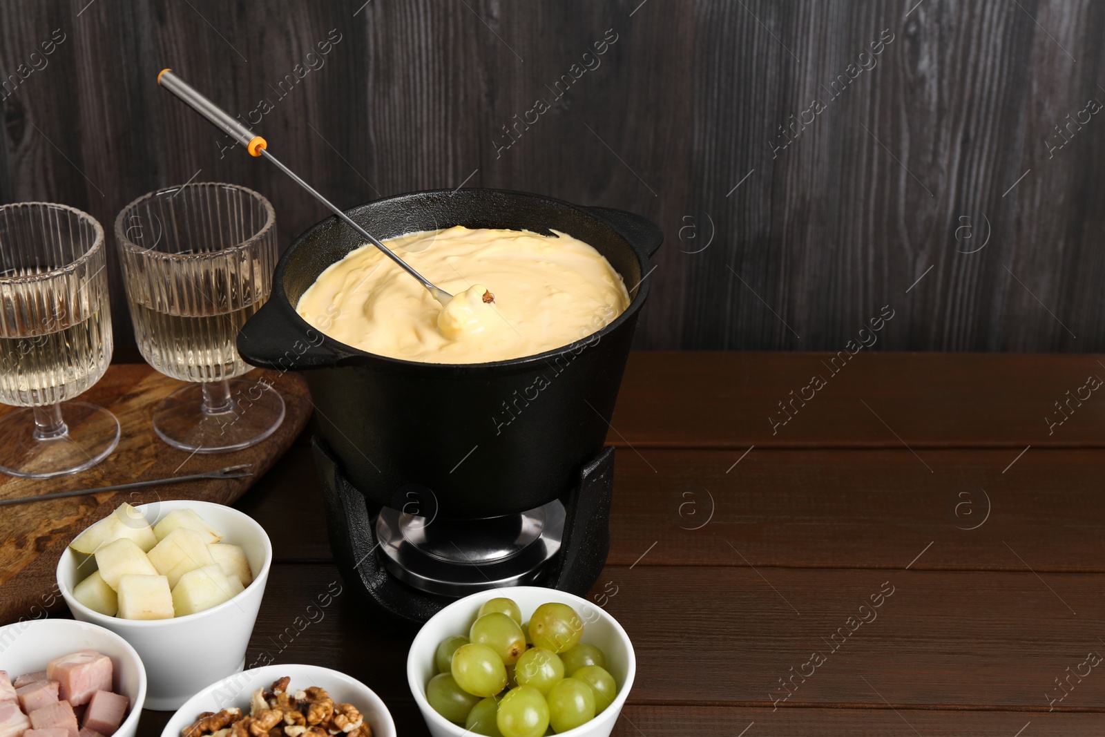 Photo of Fondue pot with tasty melted cheese, forks, wine and different snacks on wooden table, space for text