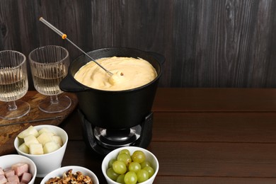 Photo of Fondue pot with tasty melted cheese, forks, wine and different snacks on wooden table, space for text