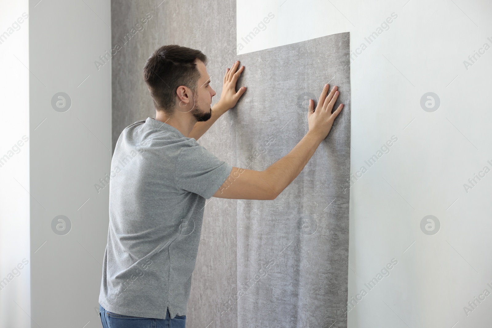 Photo of Man hanging stylish gray wallpaper in room