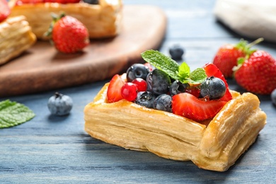 Fresh delicious puff pastry with sweet berries on blue wooden table, closeup