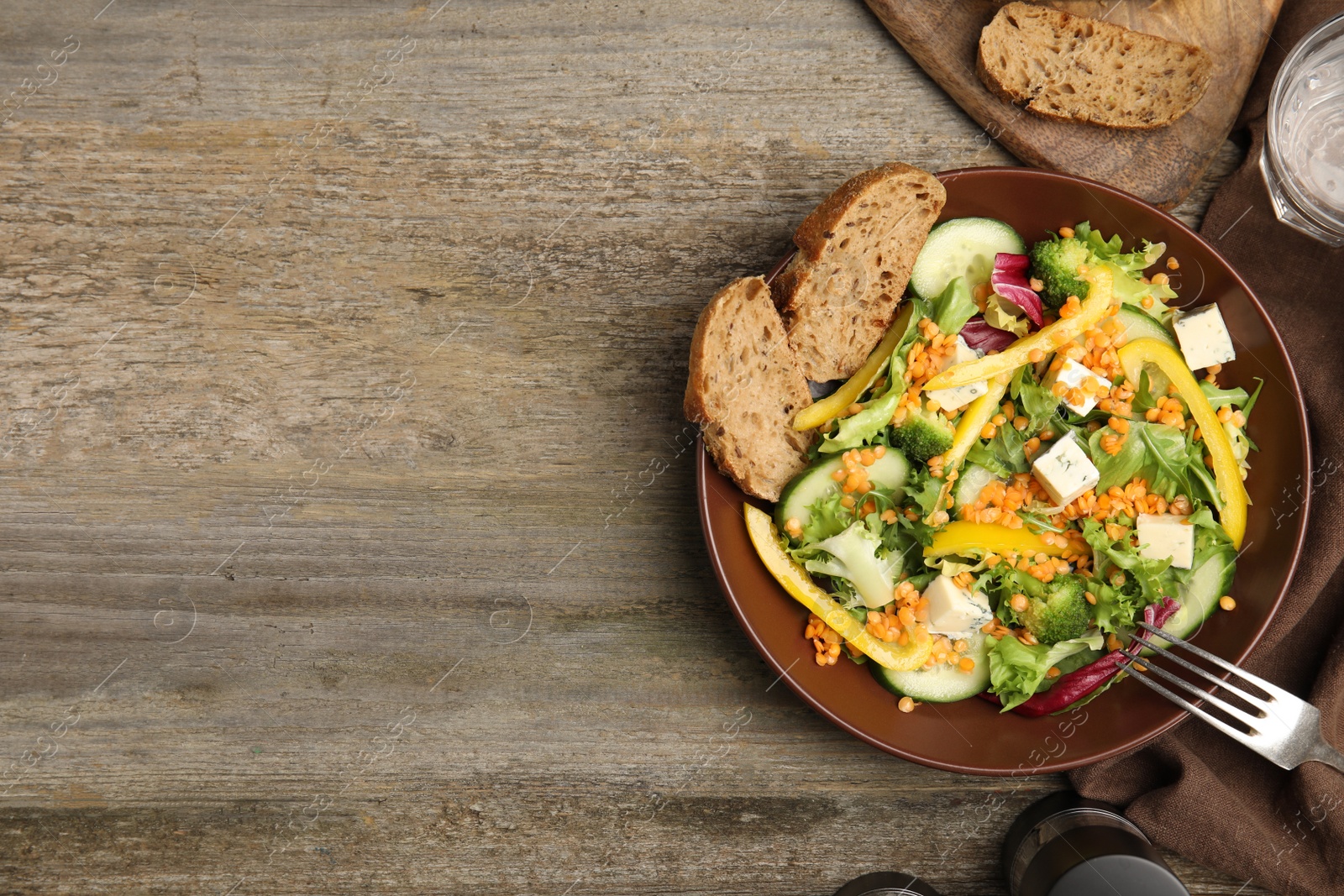 Photo of Delicious salad with lentils, vegetables and bread served on wooden table, flat lay. Space for text