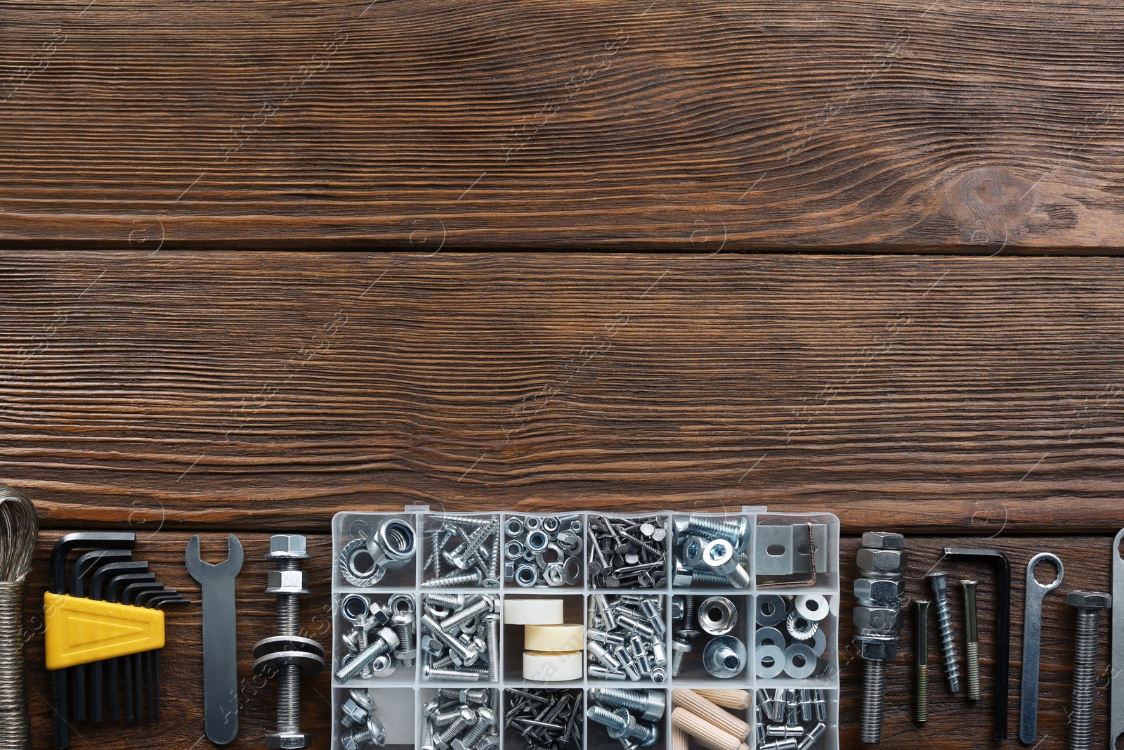 Photo of Box with different furniture fittings and tools on wooden table, flat lay. Space for text