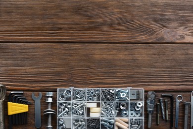 Box with different furniture fittings and tools on wooden table, flat lay. Space for text