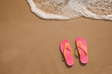 Photo of Bright pink beach slippers on sand near sea, top view. Space for text