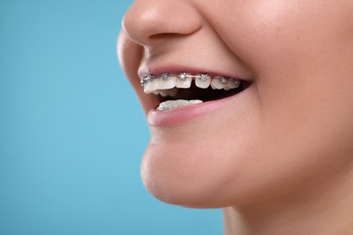 Photo of Happy woman with dental braces on light blue background, closeup. Space for text