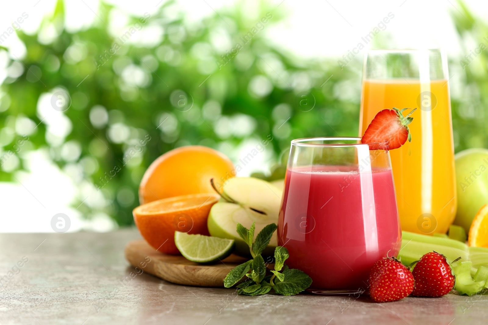 Photo of Glasses with different juices and fresh fruits on table against blurred background. Space for text