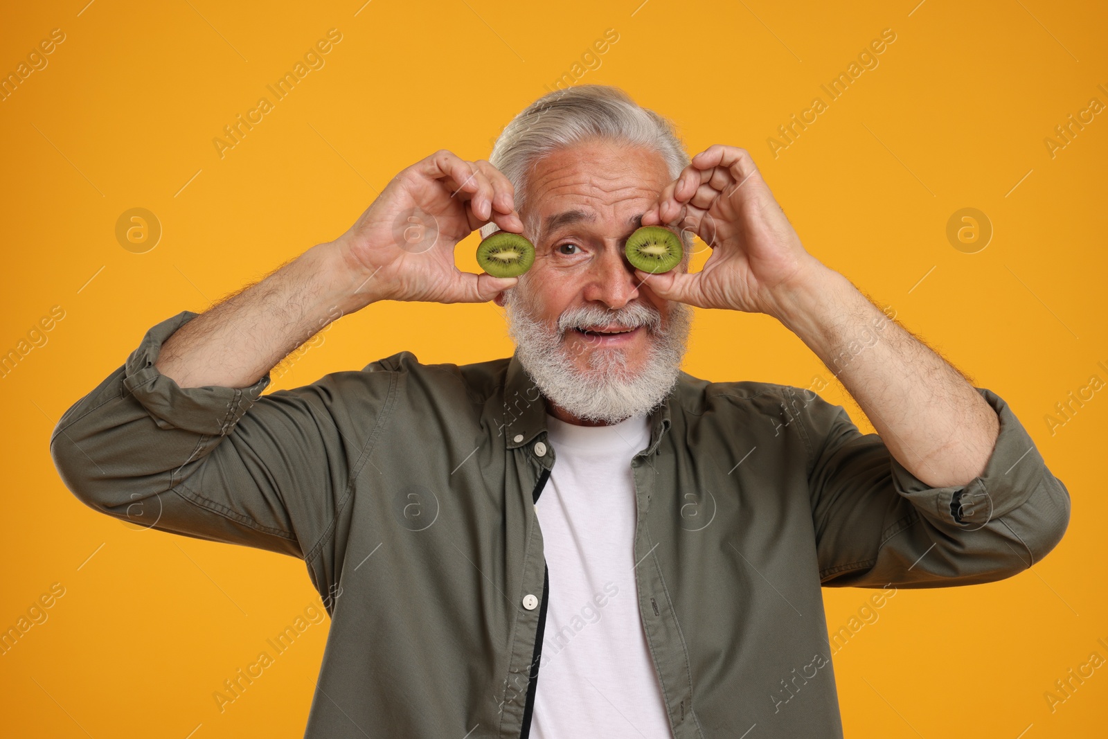 Photo of Senior man holding halves of kiwi on orange background