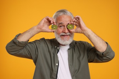 Senior man holding halves of kiwi on orange background