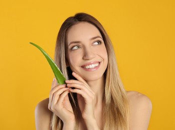 Photo of Happy young woman with aloe leaf on yellow background