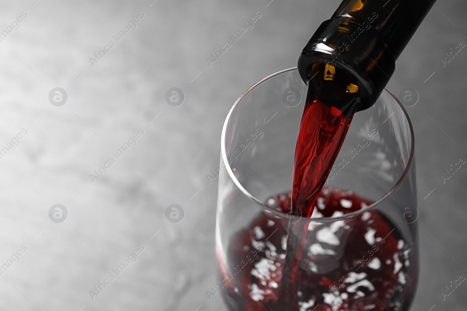 Photo of Pouring red wine from bottle into glass on grey background, closeup. Space for text