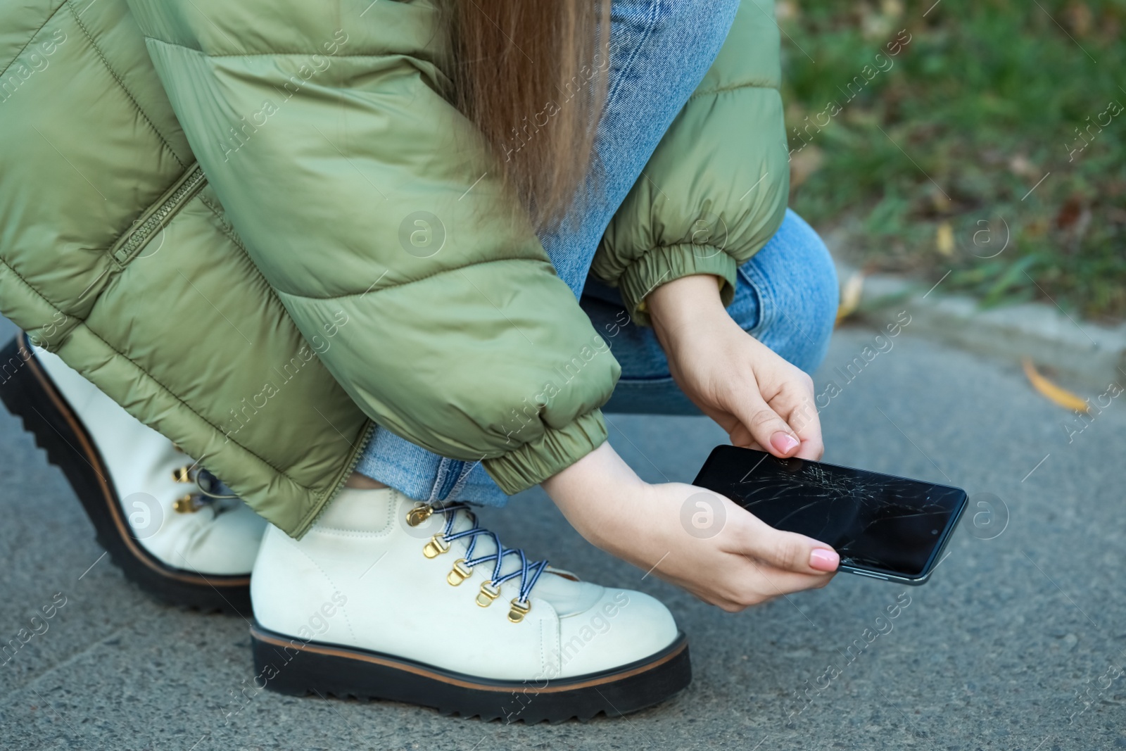 Photo of Woman taking dropped smartphone from asphalt outdoors, closeup. Device repairing