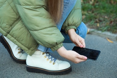 Woman taking dropped smartphone from asphalt outdoors, closeup. Device repairing