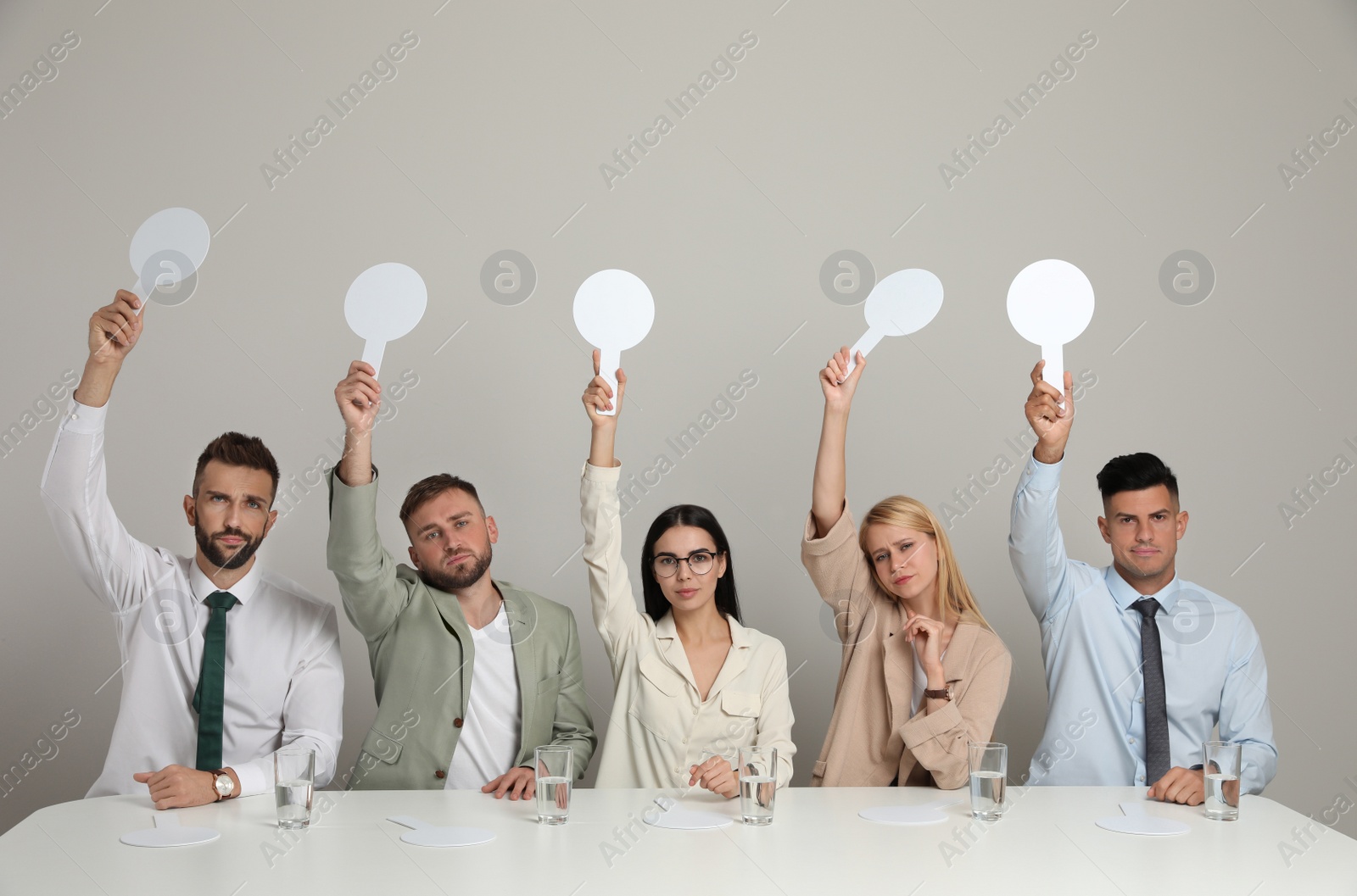 Photo of Panel of disappointed judges holding blank score signs at table on beige background. Space for text