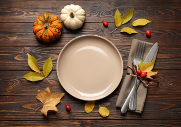 Festive table setting with autumn leaves and pumpkins on wooden background, flat lay. Thanksgiving Day celebration