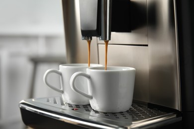 Photo of Espresso machine pouring coffee into cups against blurred background, closeup