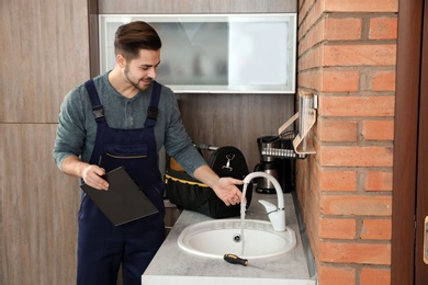 Male plumber in uniform checking faucet in kitchen. Repair service