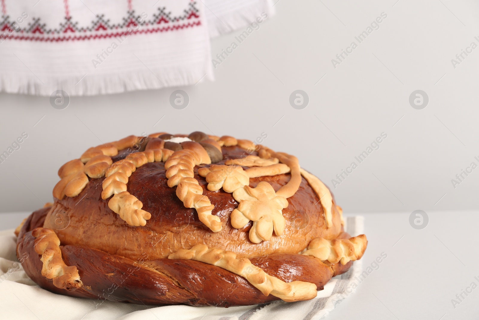 Photo of Korovai on white table against light background. Ukrainian bread and salt welcoming tradition