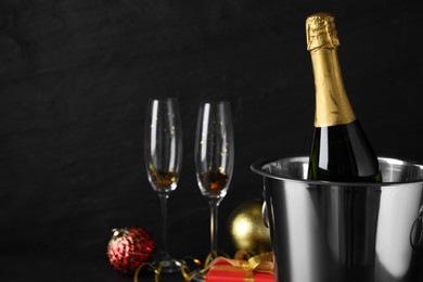 Photo of Happy New Year! Bottle of sparkling wine in bucket and glasses on black background