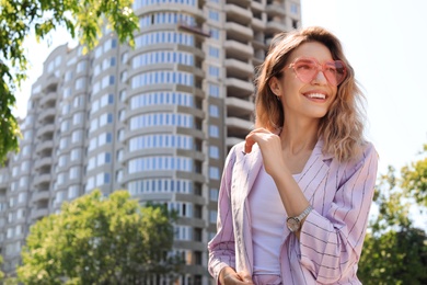 Photo of Portrait of happy young woman with heart shaped glasses in city on sunny day. Space for text