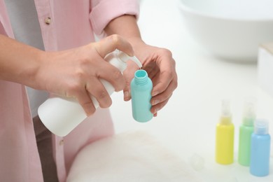 Photo of Woman pouring cosmetic product into plastic bottle over white countertop indoors, closeup and space for text. Bath accessories