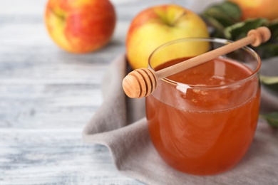 Glass of honey, apples and dipper on wooden table