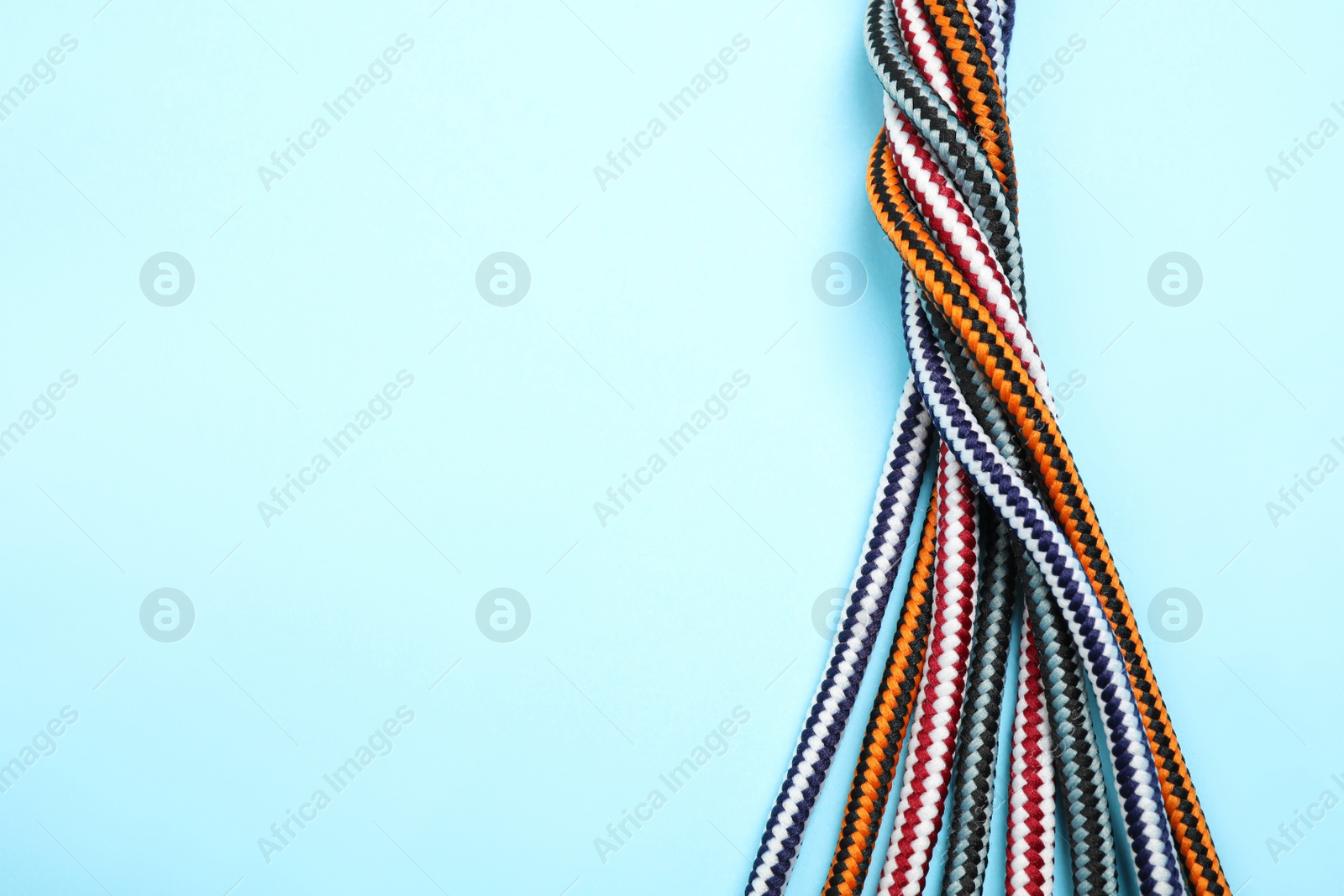 Photo of Top view of twisted colorful ropes on light blue background, space for text. Unity concept