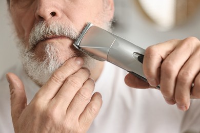 Photo of Man trimming mustache with electric trimmer indoors, closeup