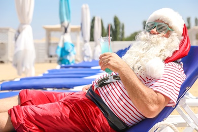 Photo of Authentic Santa Claus with cocktail resting on lounge chair at resort