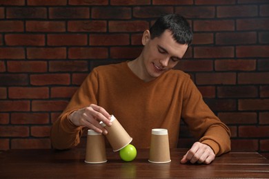 Photo of Shell game. Man showing ball under cup at wooden table