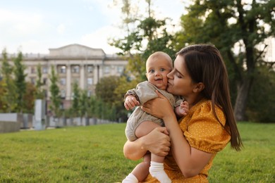 Happy mother with adorable baby walking in park on sunny day, space for text