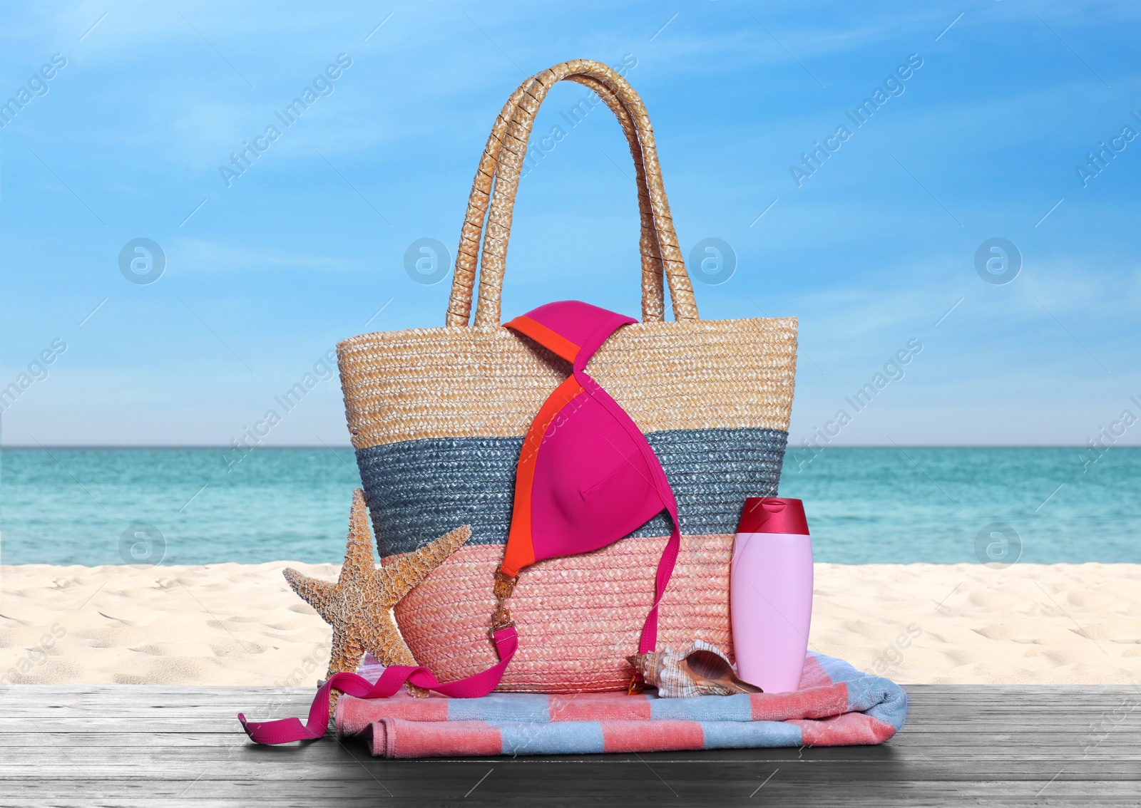 Image of Stylish bag and other beach accessories on wooden table near sea