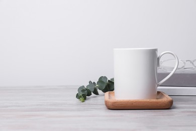 Photo of White ceramic mug, stack of books and eucalyptus branch on white wooden table, space for text