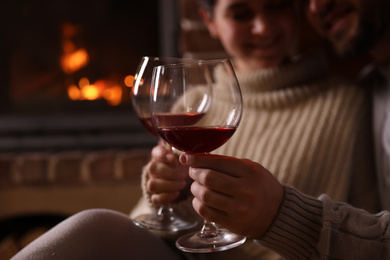 Photo of Lovely couple with glasses of wine near fireplace at home, focus on hands. Winter vacation