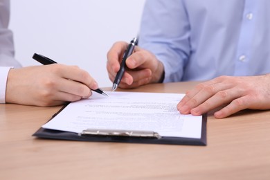 Photo of Businesspeople signing contract at wooden table, closeup of hands