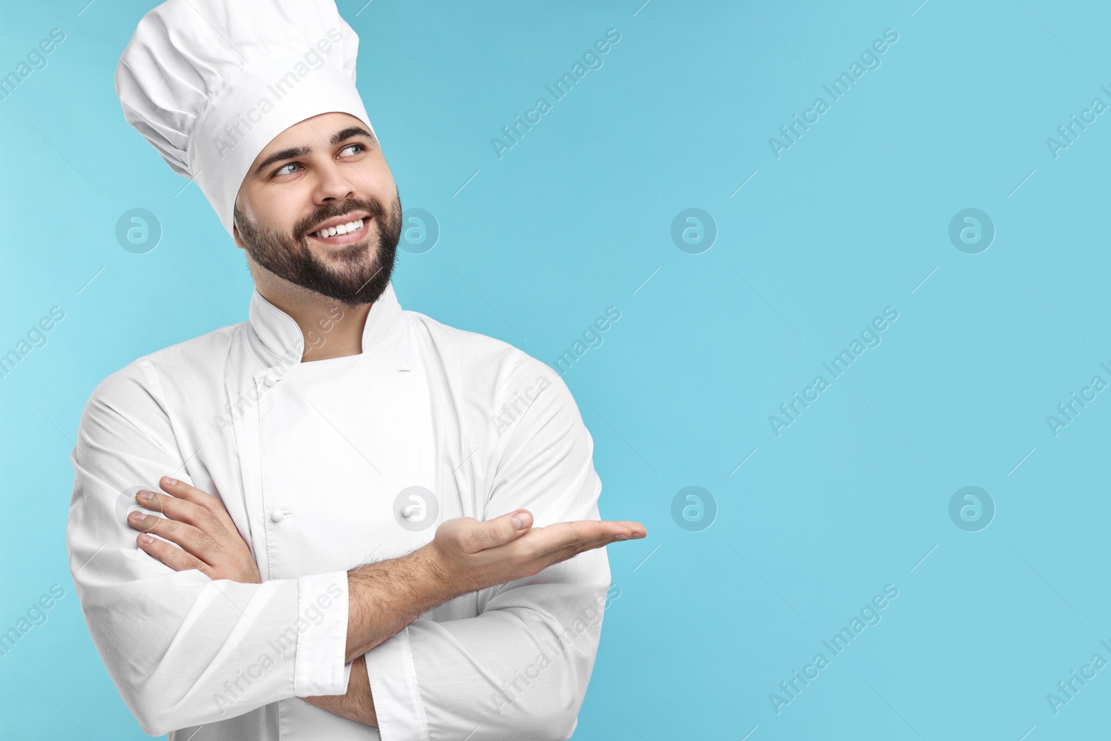 Photo of Happy young chef in uniform on light blue background. Space for text