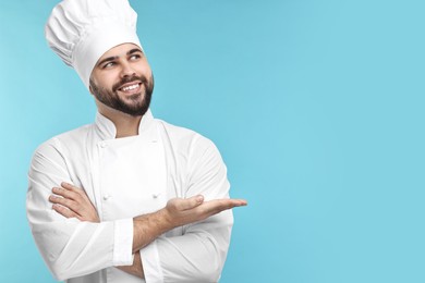 Happy young chef in uniform on light blue background. Space for text