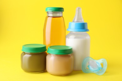 Photo of Healthy baby food, juice, milk and pacifier on yellow background