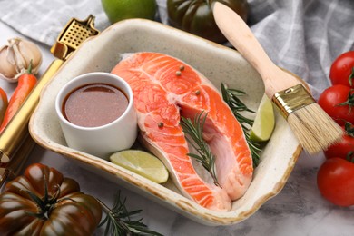 Fresh fish, lime, rosemary, marinade in baking dish and other products on table, closeup