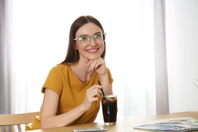 Photo of Young woman with glass of cola at table indoors. Refreshing drink