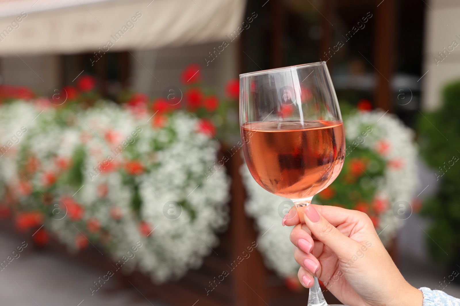 Photo of Woman holding glass of rose wine outdoors, closeup. Space for text