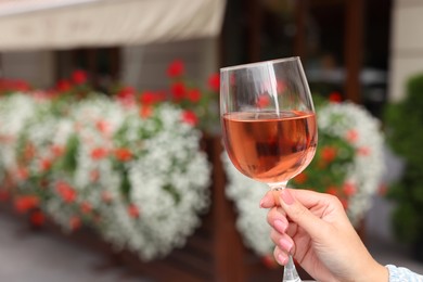 Photo of Woman holding glass of rose wine outdoors, closeup. Space for text