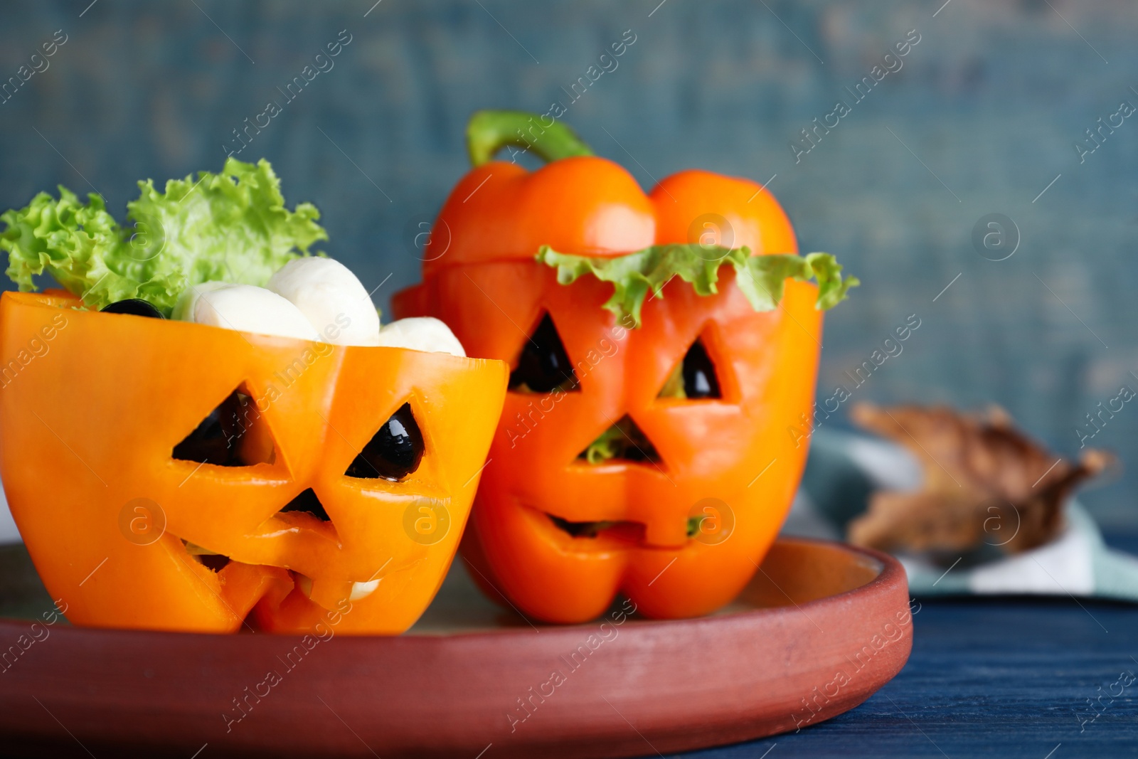 Photo of Bell peppers with black olives and lettuce as Halloween monsters on blue wooden table, closeup