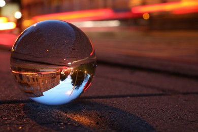 Photo of Beautiful city street, overturned reflection. Crystal ball on asphalt road at night. Space for text