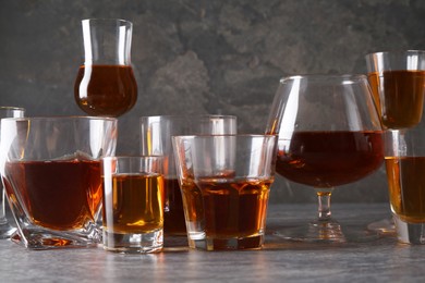 Many different liqueurs in glasses on grey textured table