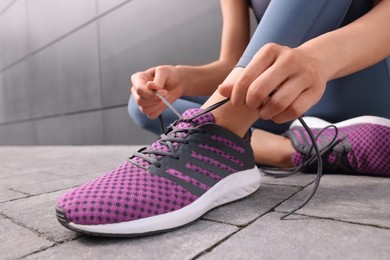 Photo of Woman tying shoelace of sneakers on street, closeup
