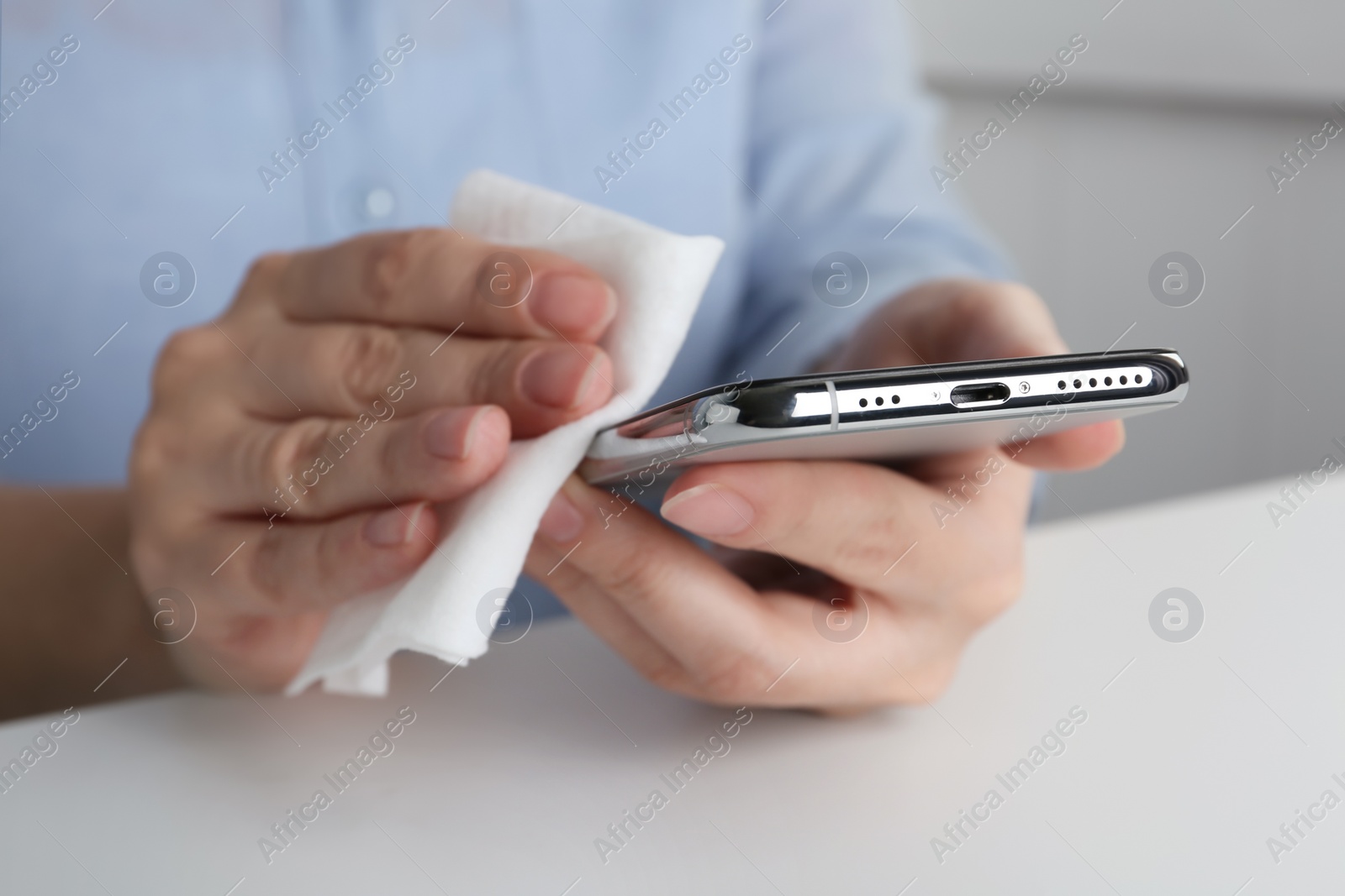 Photo of Woman cleaning smartphone with antiseptic wipe at white table, closeup