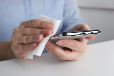 Photo of Woman cleaning smartphone with antiseptic wipe at white table, closeup